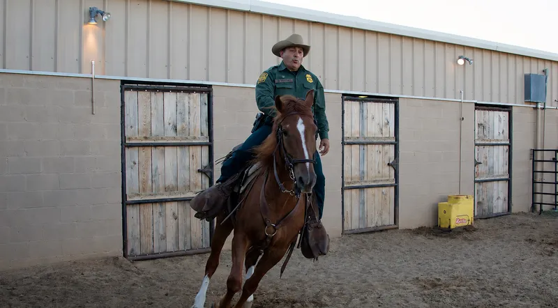 A mounted Border Patrol agent riding beside a stable