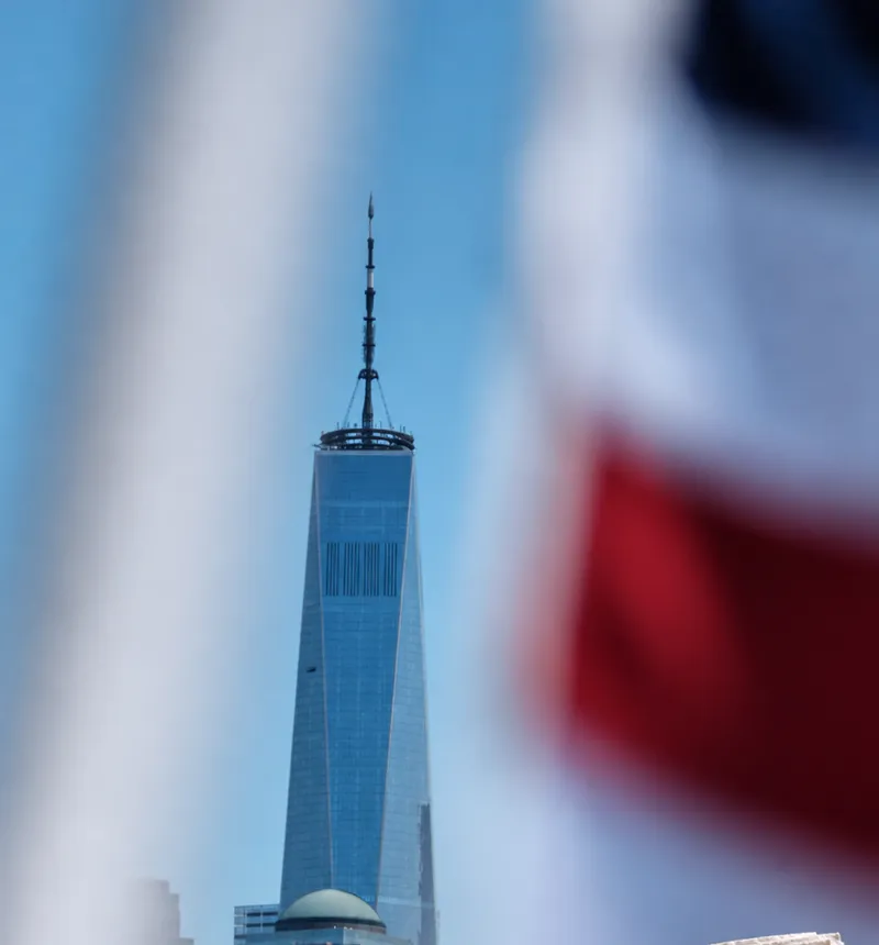 One World Trade Center against a blue sky, seen through a blurred American flag