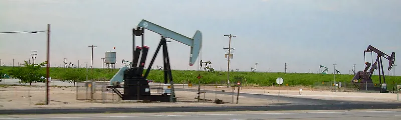 Oil pumpjacks across a flat field beside a highway